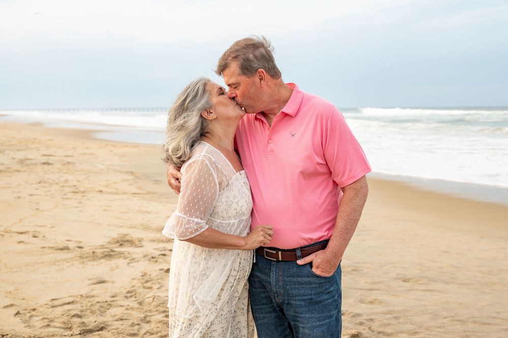 Couple sharing romantic moments on a sandy beach with ocean waves in the background.