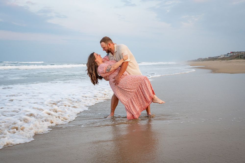 A couple in coordinating coral outfits plays together in the ocean waves at the beach during sunset.