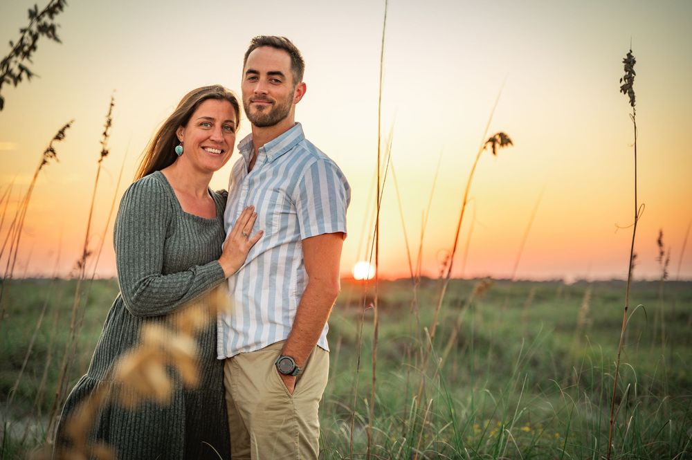 Couple enjoying a romantic sunset photoshoot in a field of tall grass during golden hour.