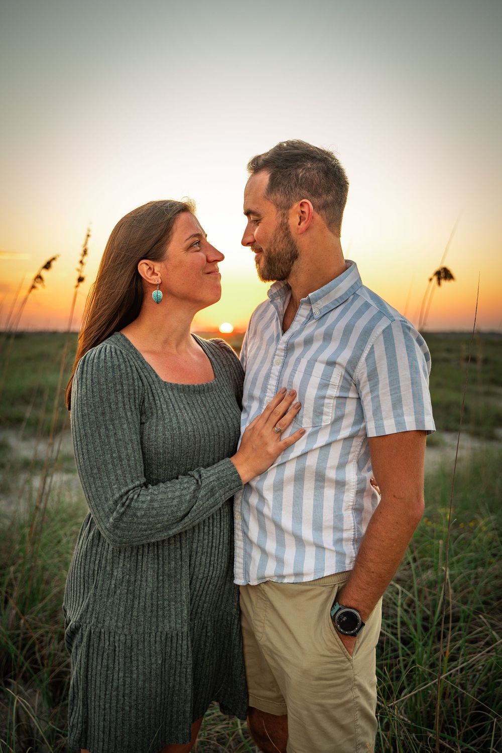 A romantic couple shares an intimate moment at sunset in a field of tall grass and sea oats.