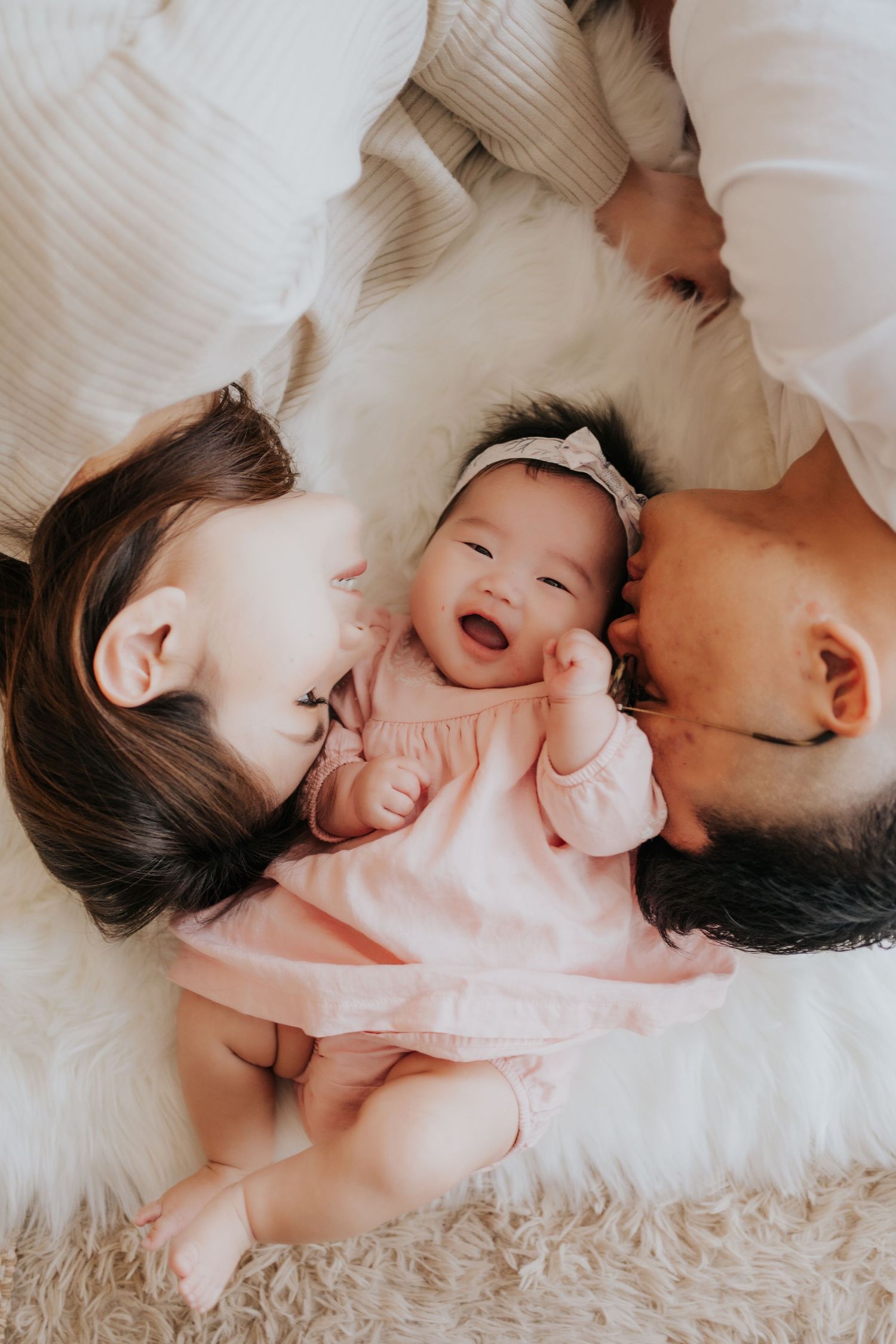 A tender family moment captured in white tones as parents share loving interactions with their baby on soft bedding.溫馨的家庭瞬間,以白色調捕捉父母與寶寶在柔軟的床