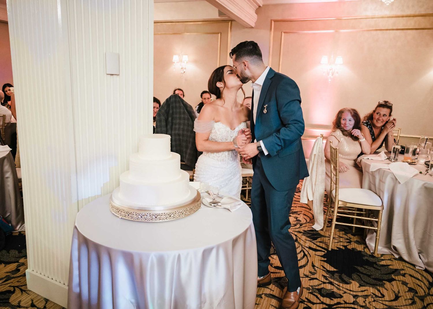 Bride and groom share a kiss beside their wedding cake during the reception at the Lenox Hotel Boston