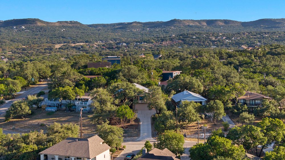 Aerial view of a residential neighborhood nestled in the Texas Hill Country with homes scattered among green trees.