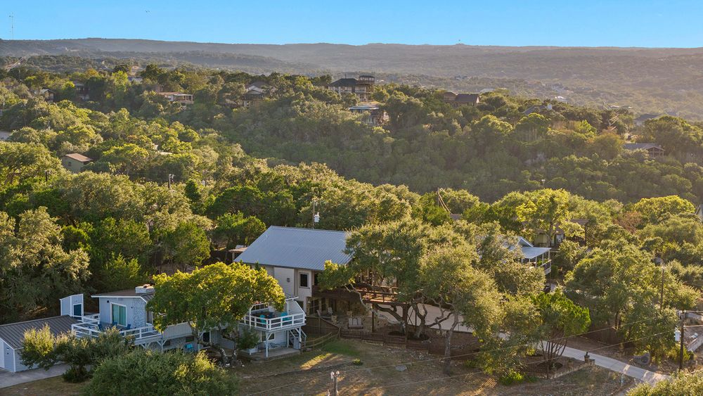 Hillside property with white house surrounded by native trees and natural terrain in rural setting.