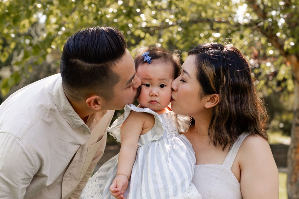 A loving family shares tender moments together in a series of outdoor portraits with natural lighting and greenery.