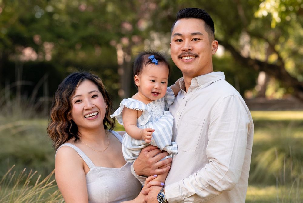 A family portrait session in a sun-dappled outdoor setting with natural lighting and casual attire.