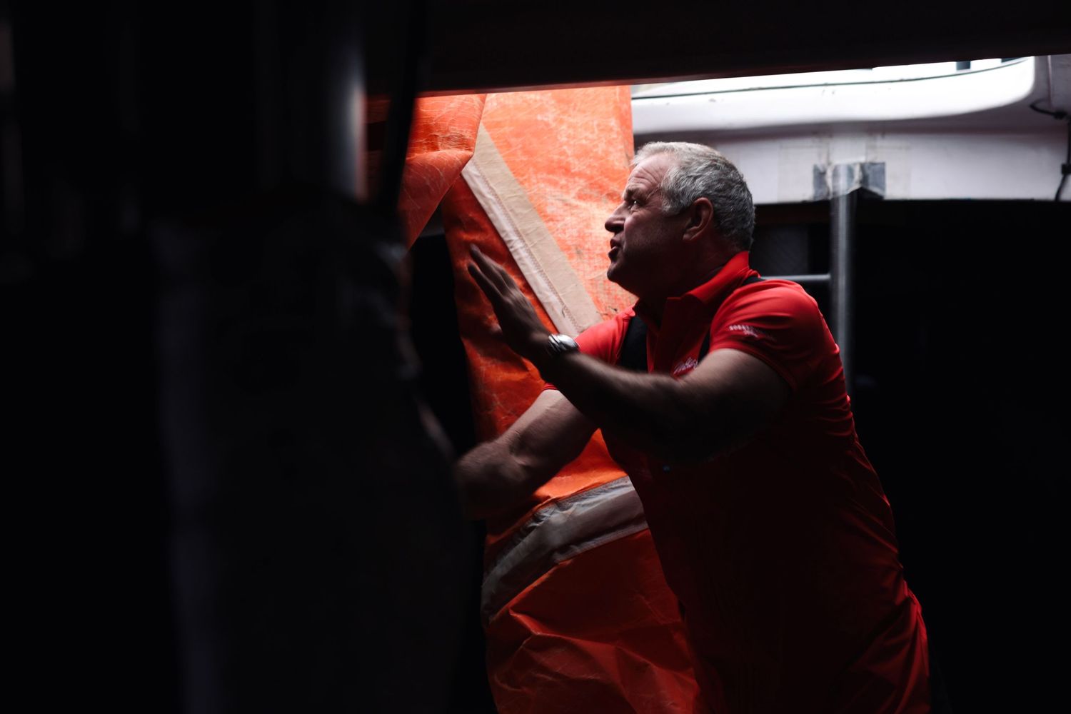 A crew member in red gear works below deck in dramatic lighting.