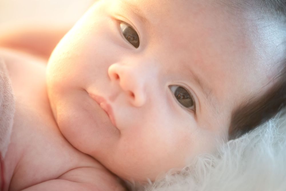 Artistic newborn photography series with baby wrapped in gray blanket against dark background.