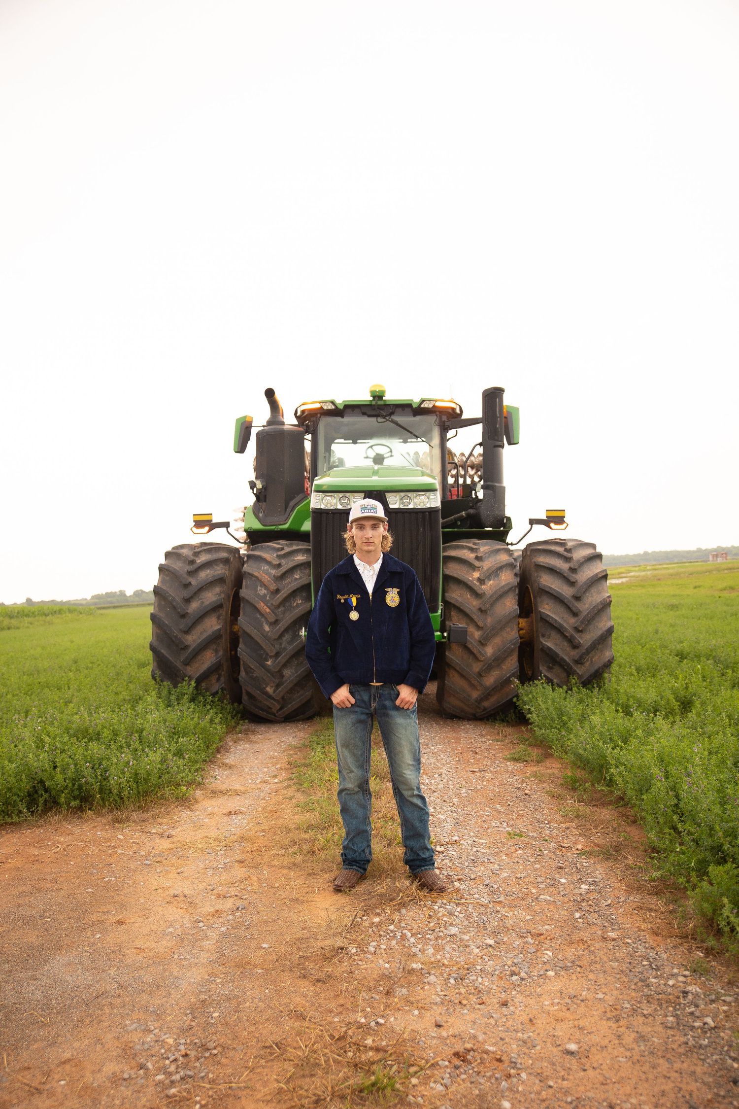 Large green John Deere tractor parked on dirt path in green field with someone standing in front.