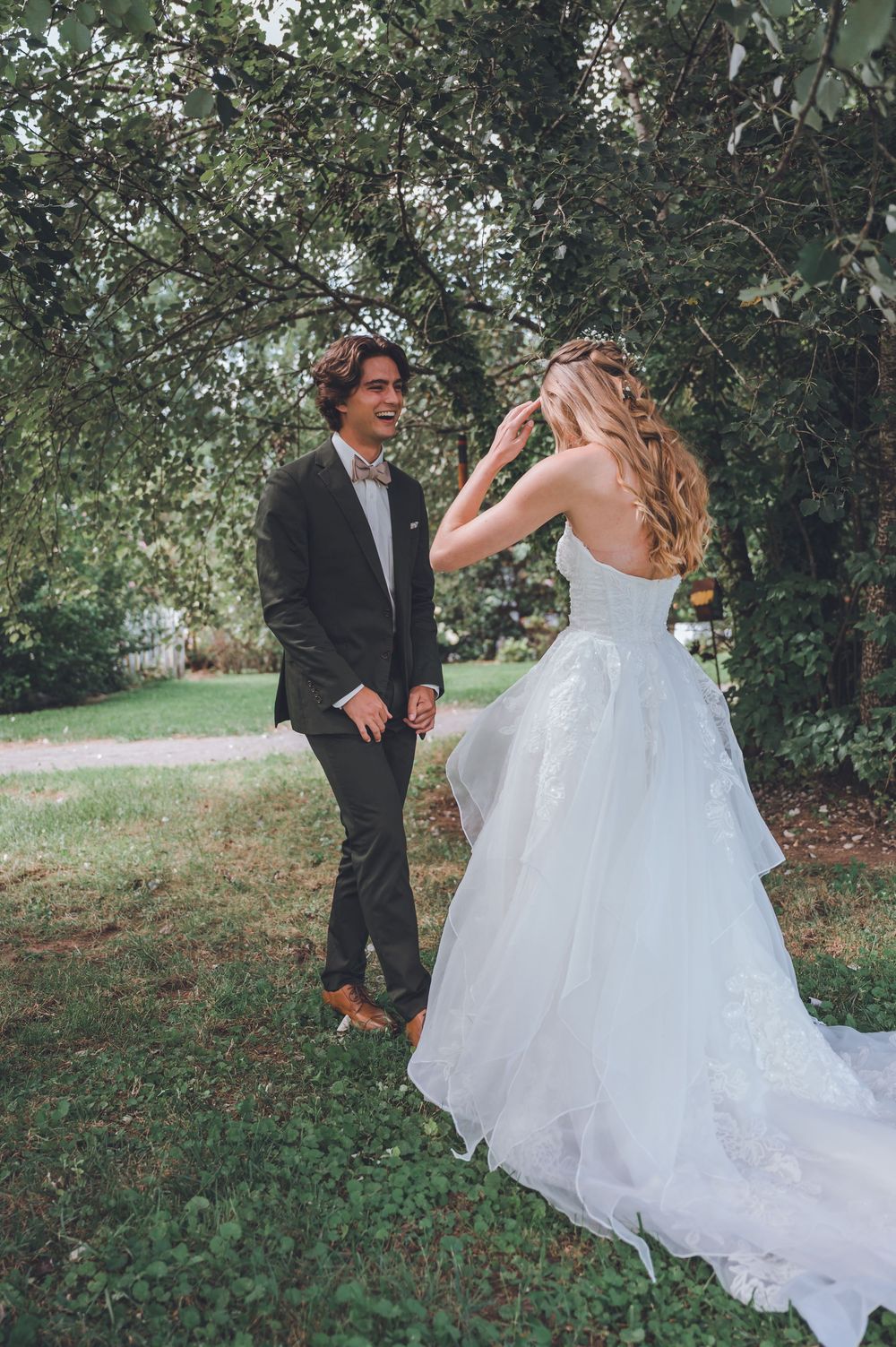 A couple in wedding attire dances and twirls playfully outdoors among trees and greenery in a candid photo sequence.