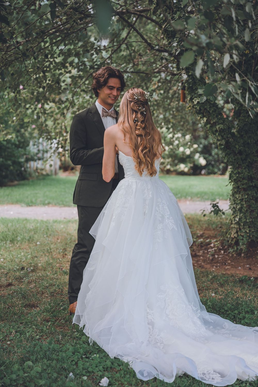 A romantic wedding couple embraces in a lush garden setting with a flowing white ballgown dress.