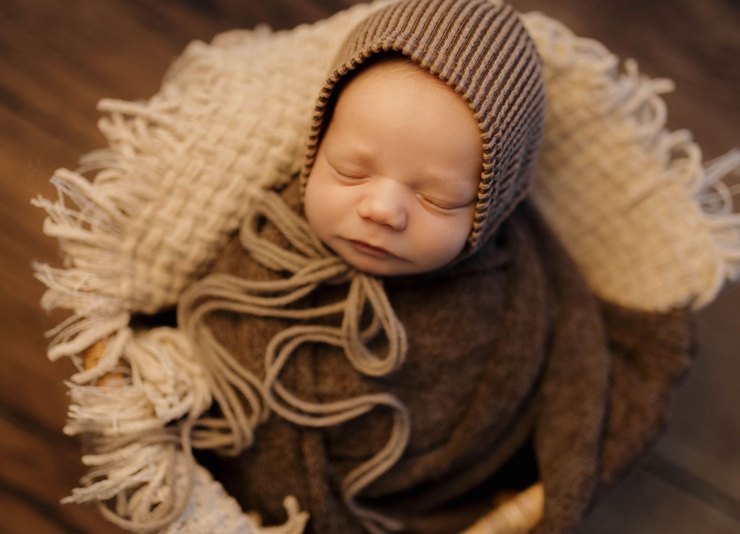 A sleeping newborn baby swaddled in brown fabric wearing a knit beanie hat.