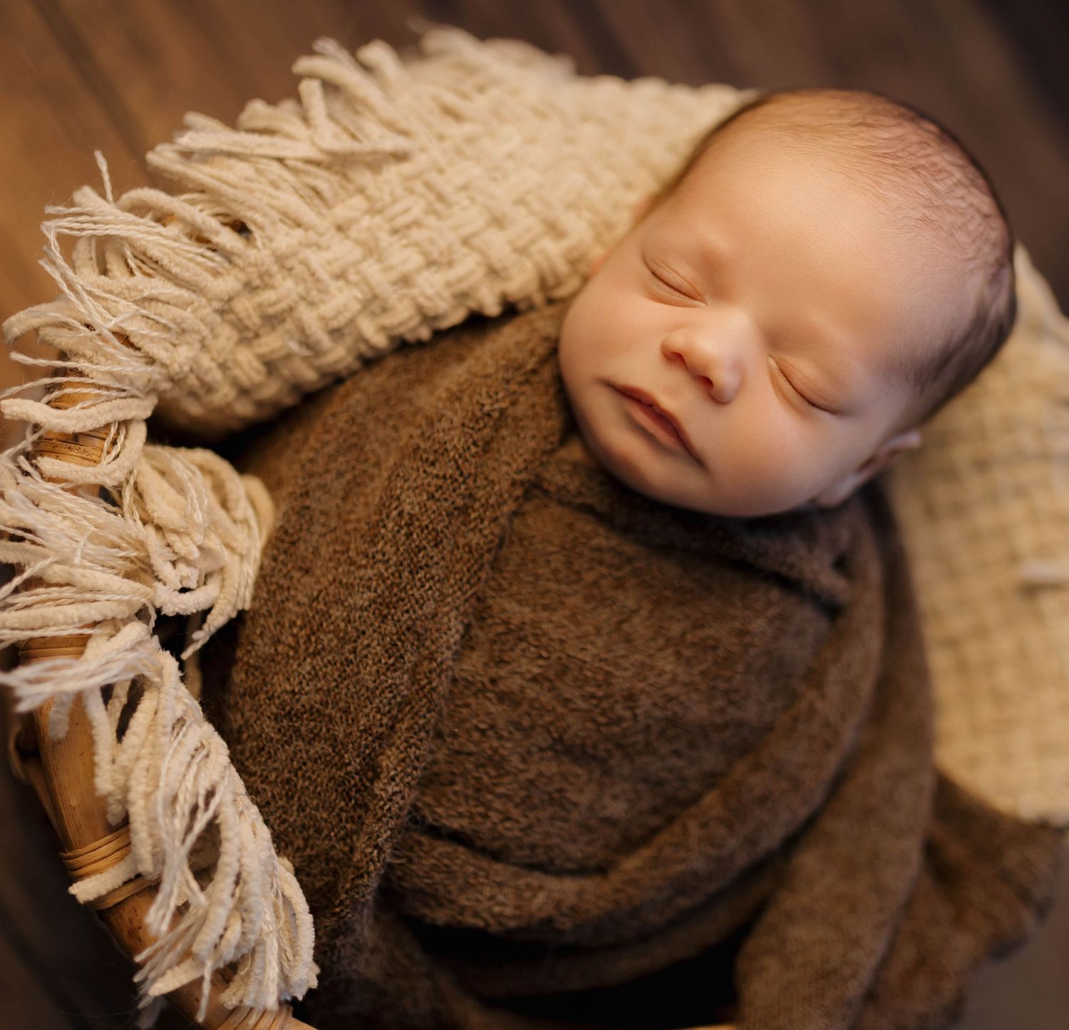 Sleeping newborn wrapped in brown swaddle with cream colored textured blanket.