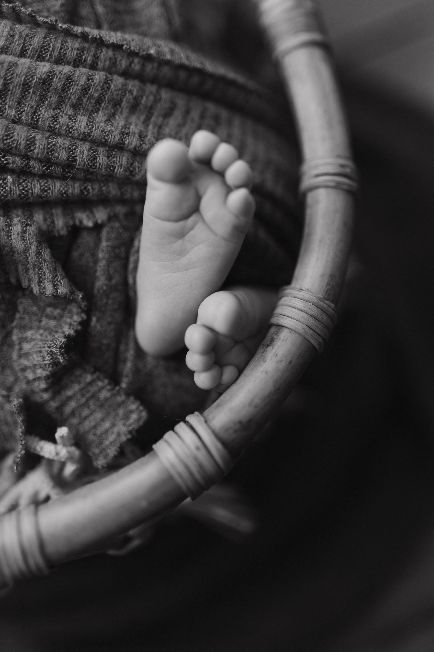 Black and white close-up of tiny baby feet resting on a wooden rocking chair with textured fabric.