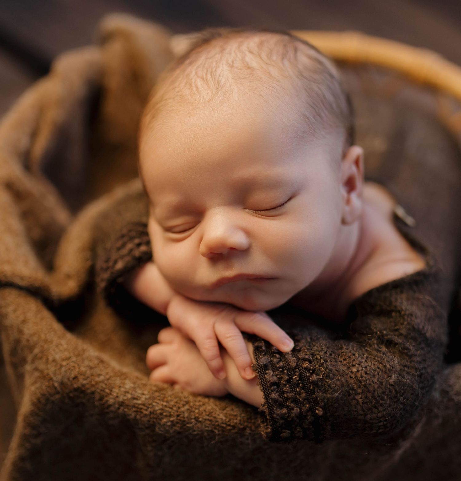 Peaceful sleeping newborn with folded hands resting on soft brown blanket.