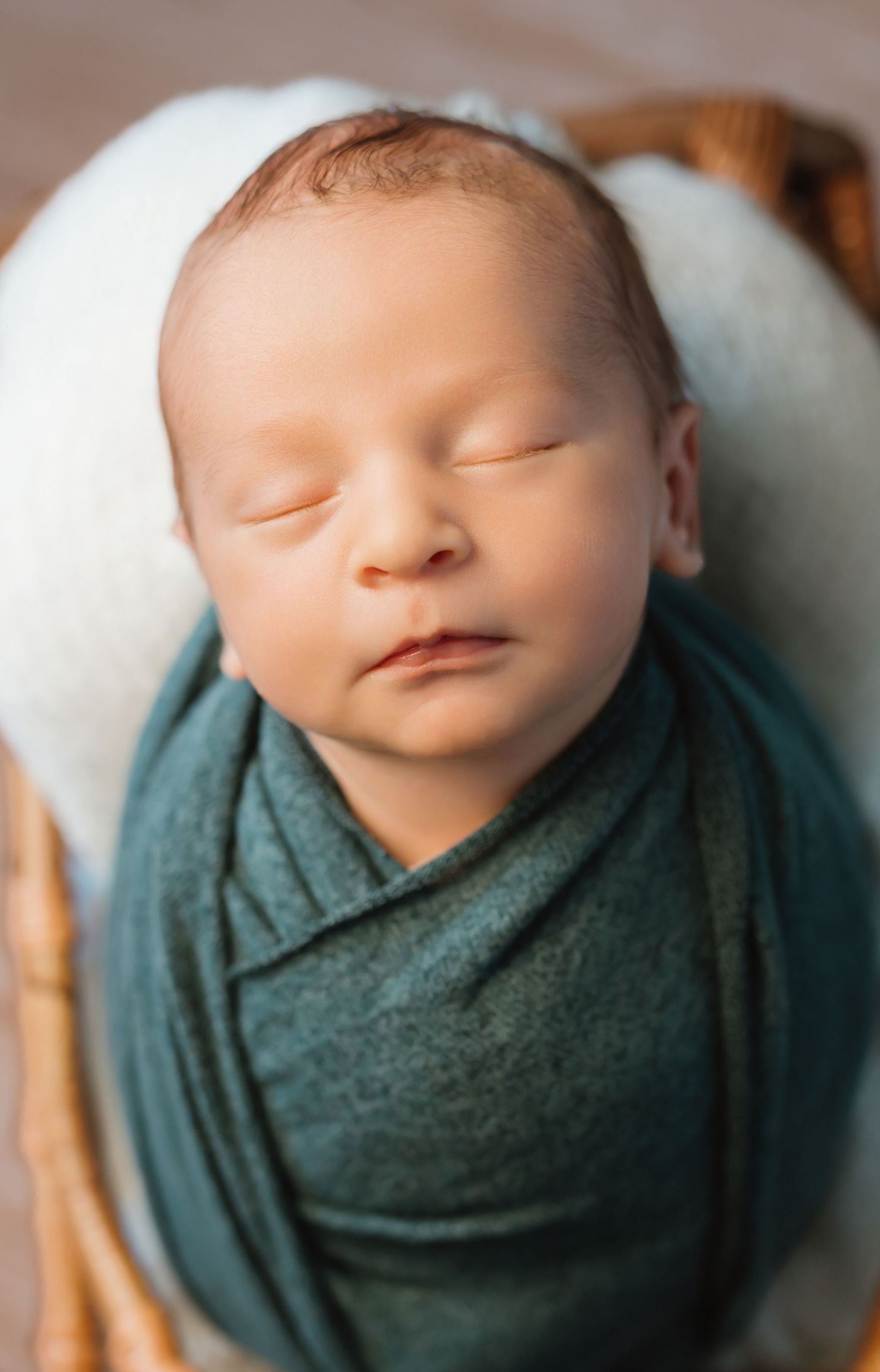 A sleeping newborn baby wrapped in a teal swaddle blanket against a soft white background.