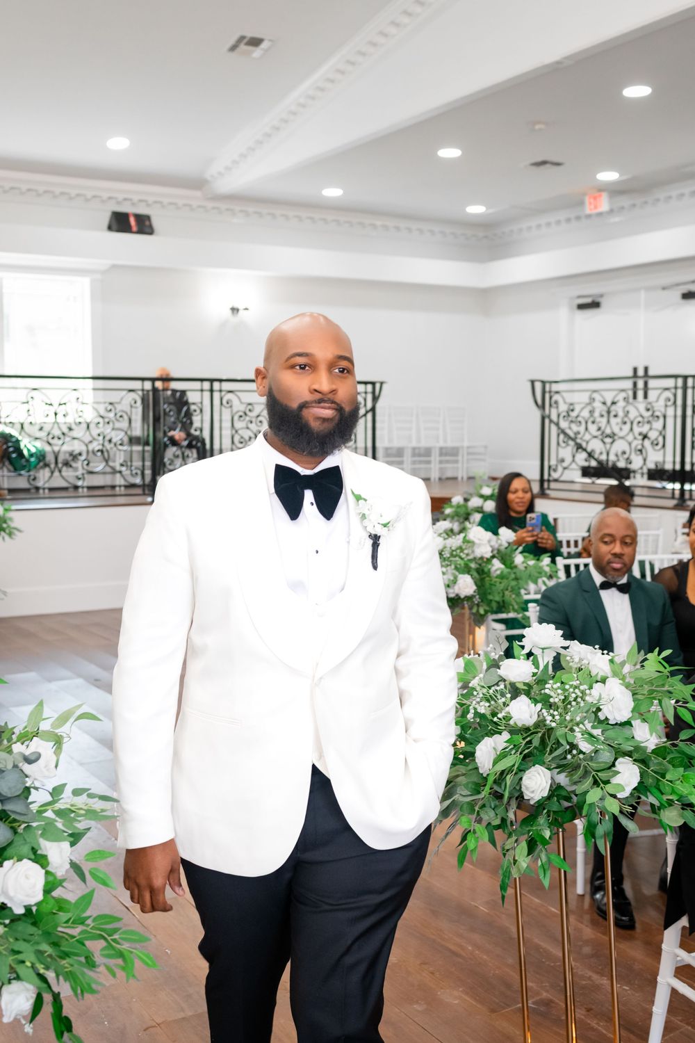 Wedding venue decorated with white floral arrangements and men in classic black and white tuxedos.