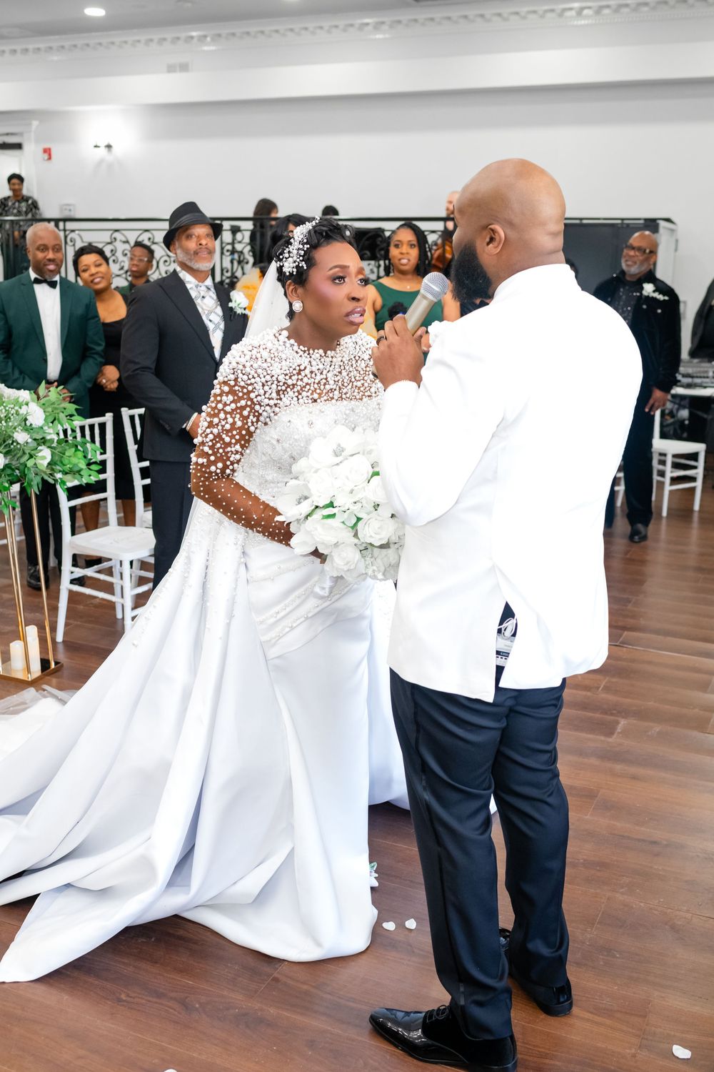 A couple dances together at a wedding reception in a bright indoor venue with white decor.