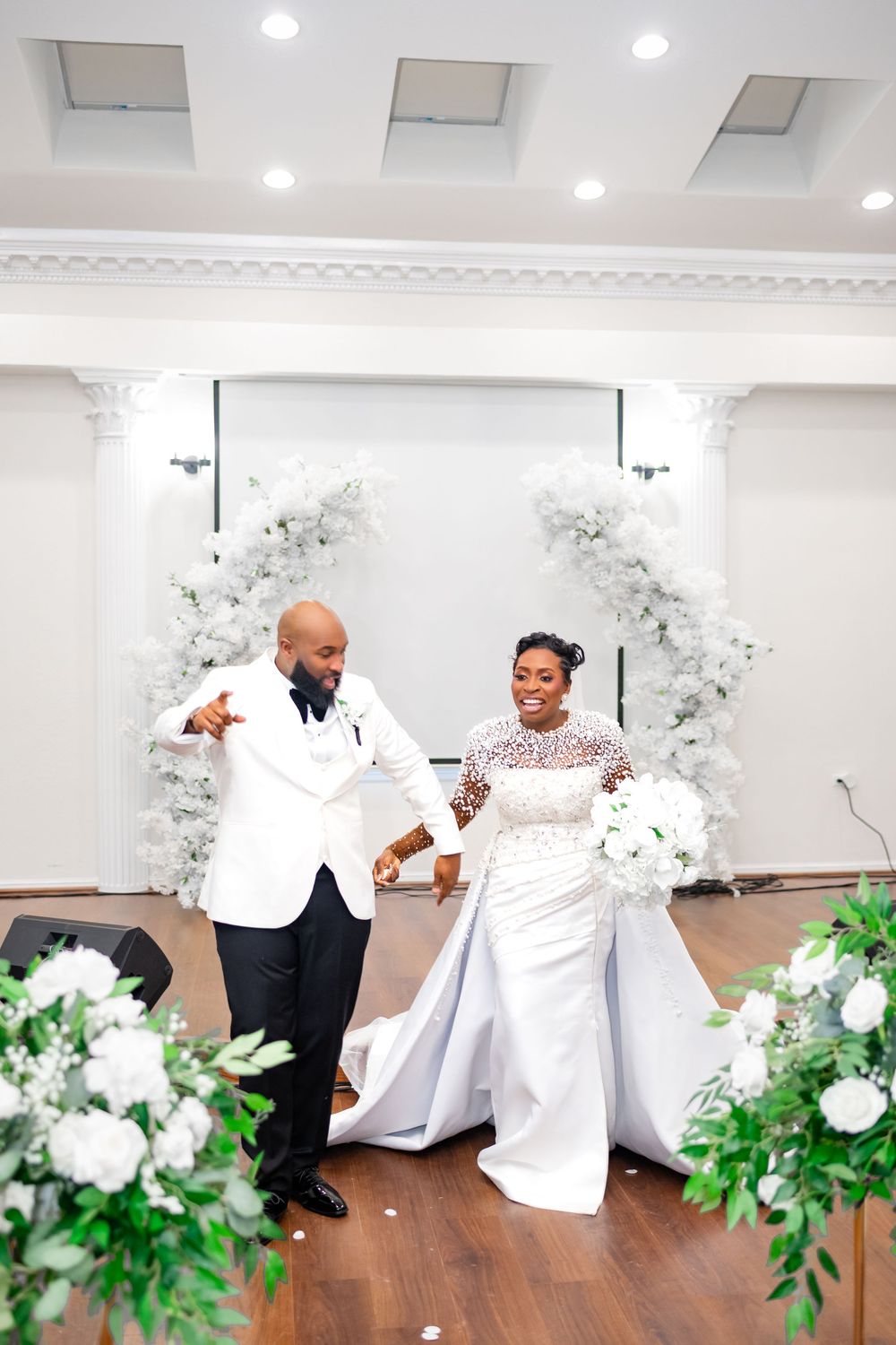 A couple shares a tender moment on the dance floor surrounded by white floral decorations.