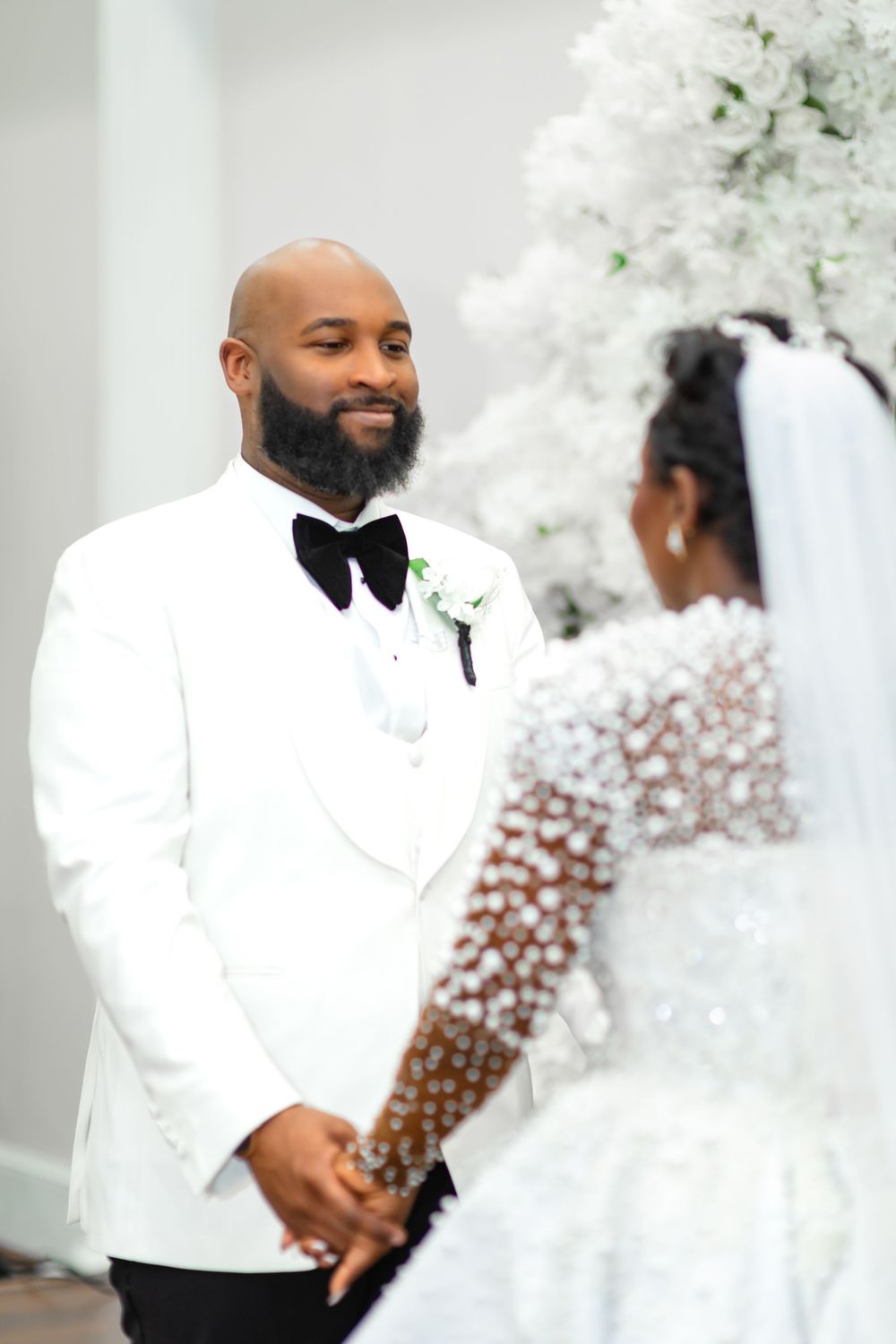 A couple in elegant white wedding attire share an intimate moment during their celebration.