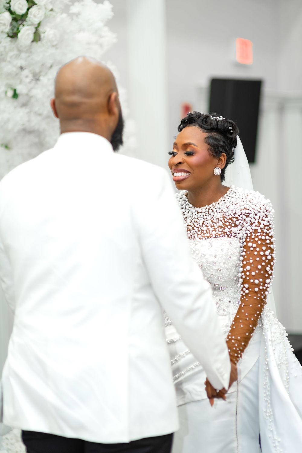 A wedding couple shares an intimate moment in front of white floral decorations at an elegant venue.