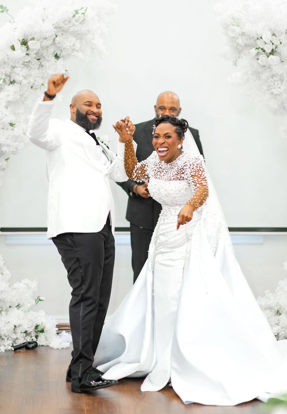 A joyful couple shares a dance together at their wedding reception surrounded by white floral decorations.