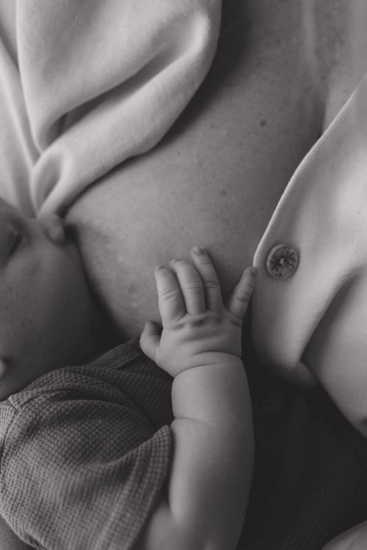 Black and white close-up photo of a baby's hand grasping soft fabric while sleeping peacefully.