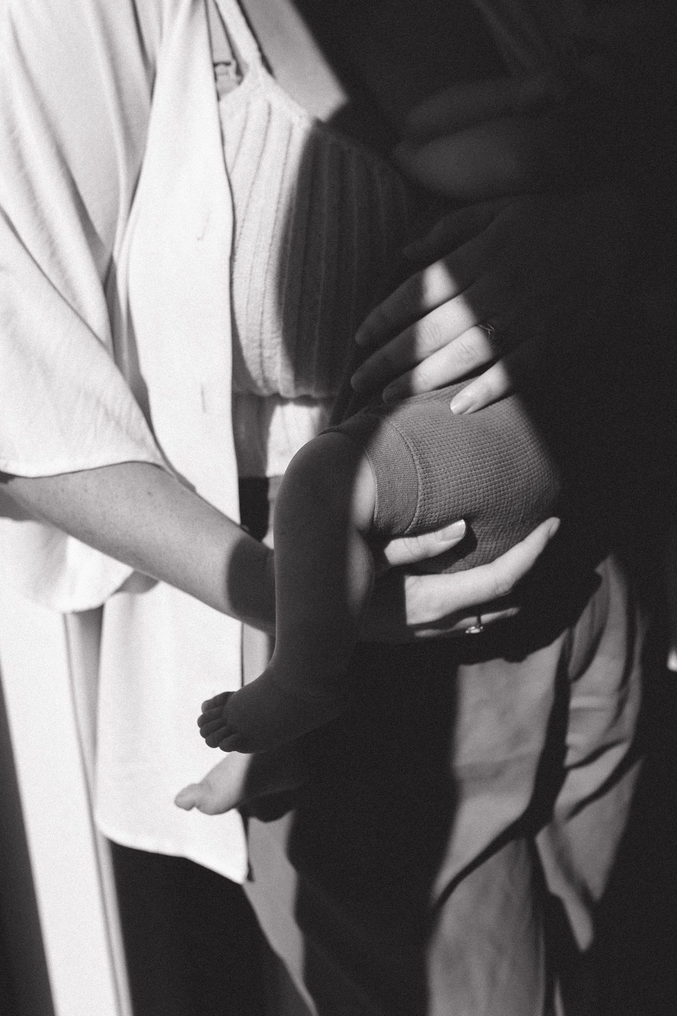 Black and white image of hands holding a football against a light background, creating dramatic shadows.