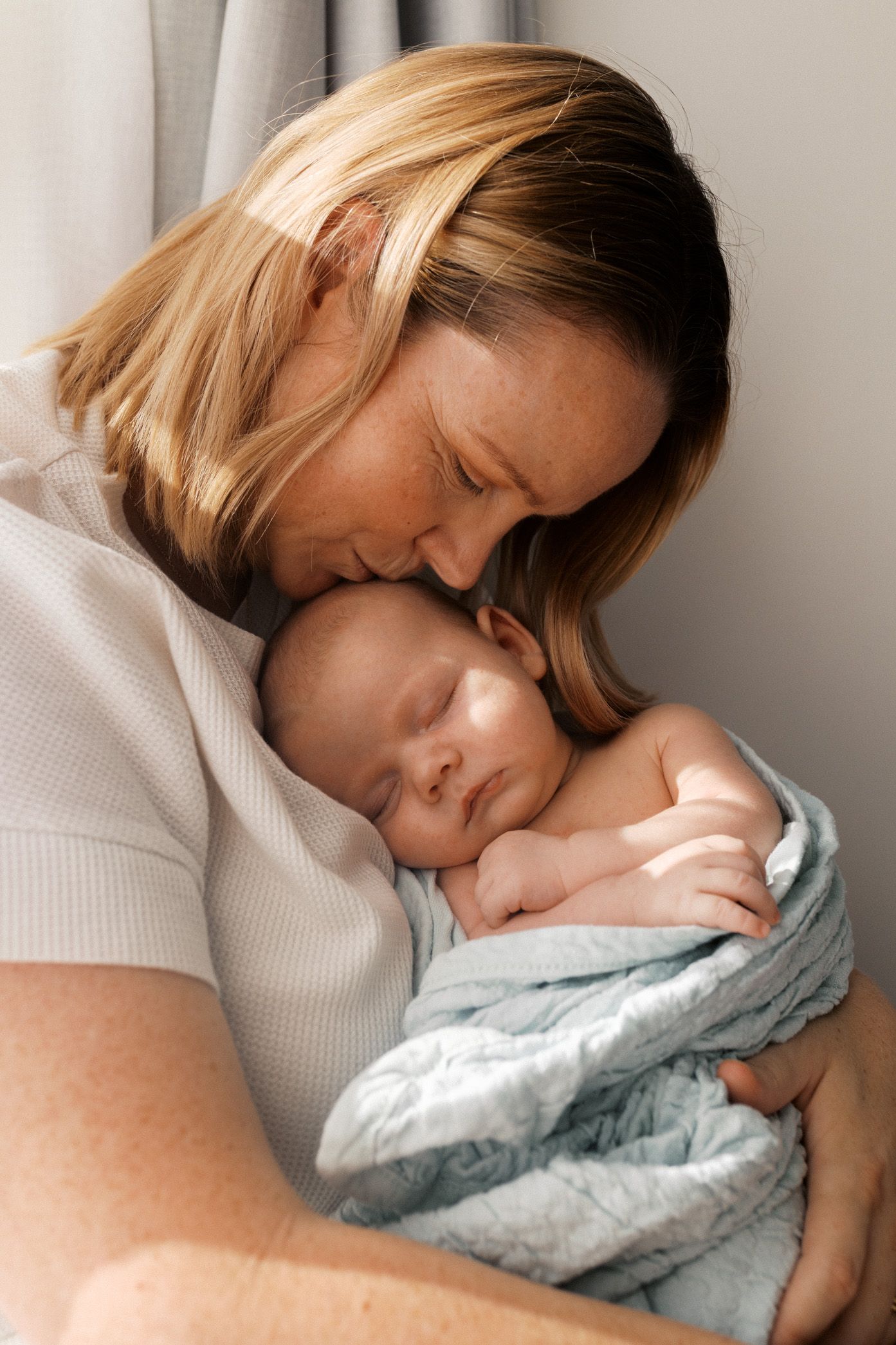 Intimate series of photos showing a parent snuggling close with a sleeping infant wrapped in a soft blue blanket.