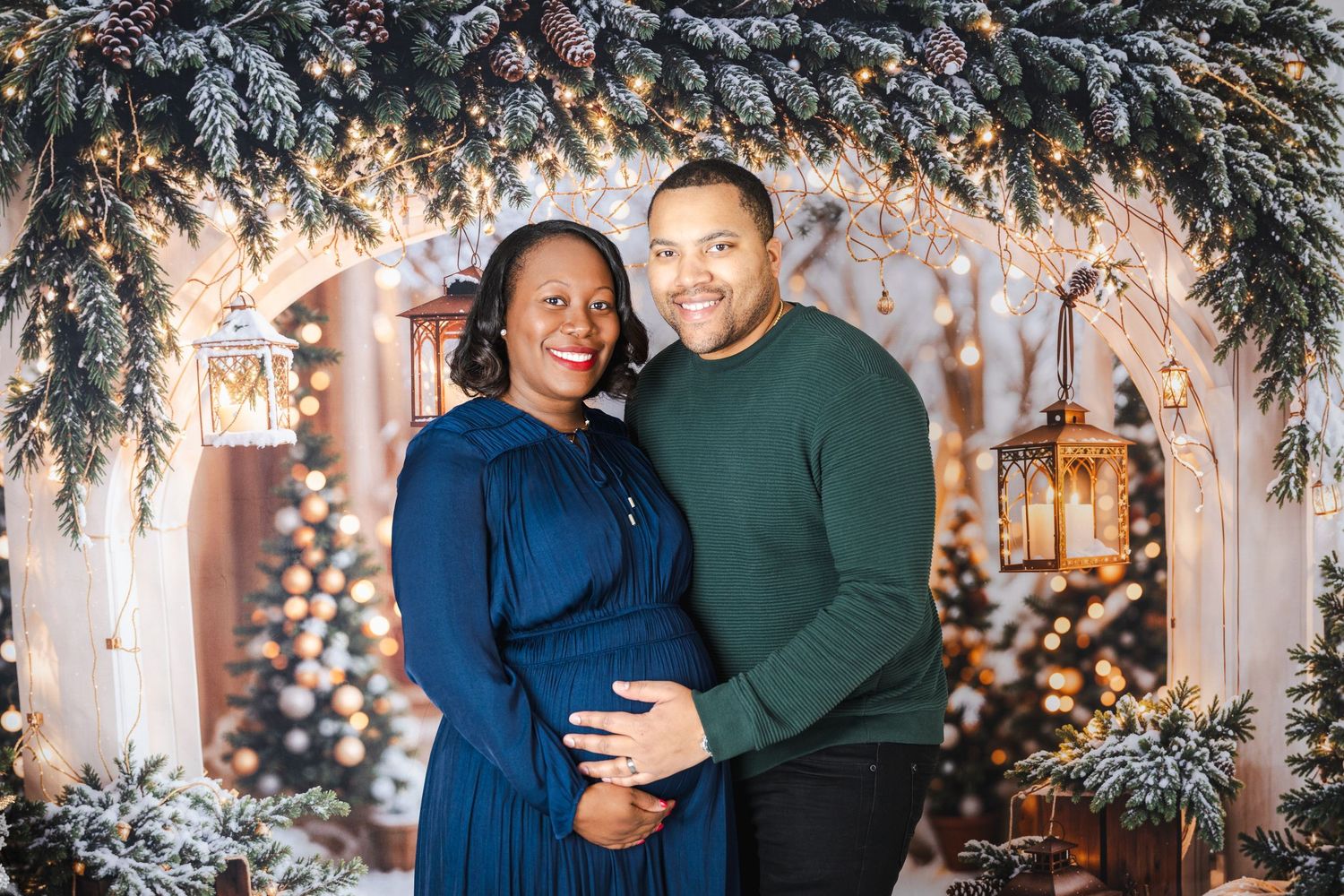 Couple in blue dress and green sweater embraces in front of holiday backdrop with twinkling lights.