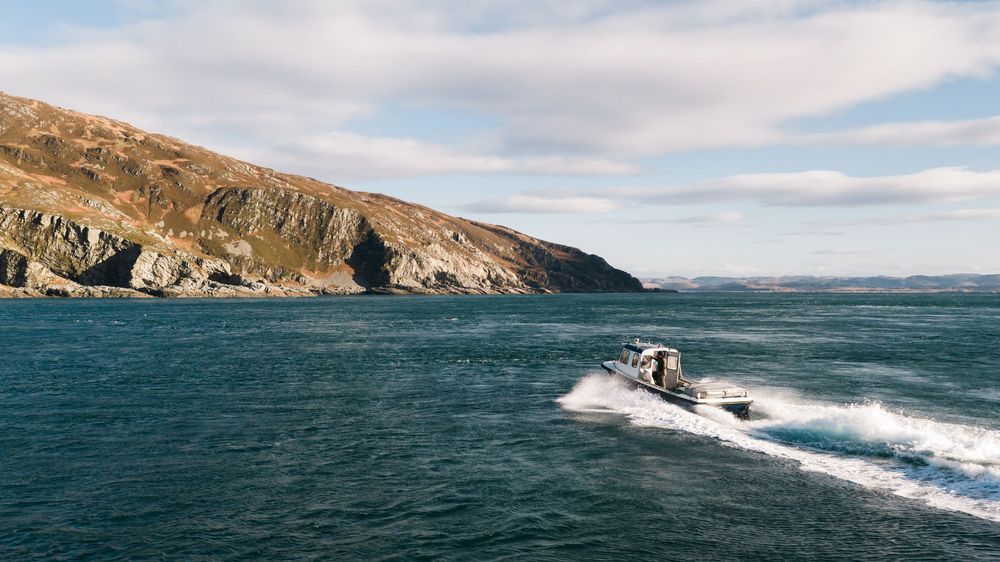 Panoramic view of a boat cruising through turquoise waters along rugged coastal cliffs under cloudy skies.