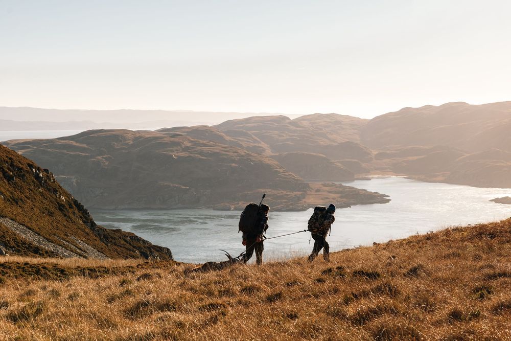 Panoramic sequence of hikers ascending a grassy mountain trail overlooking a serene coastal landscape at sunset.