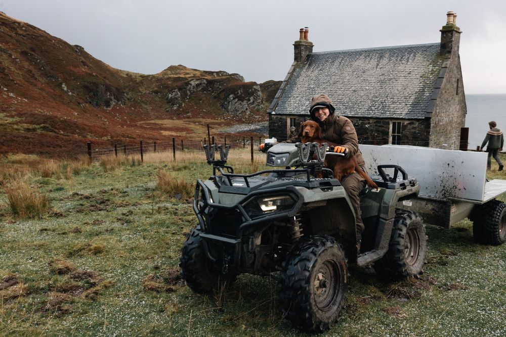 Vintage military Jeep parked near a rustic stone cottage in a remote mountainous landscape at dusk.