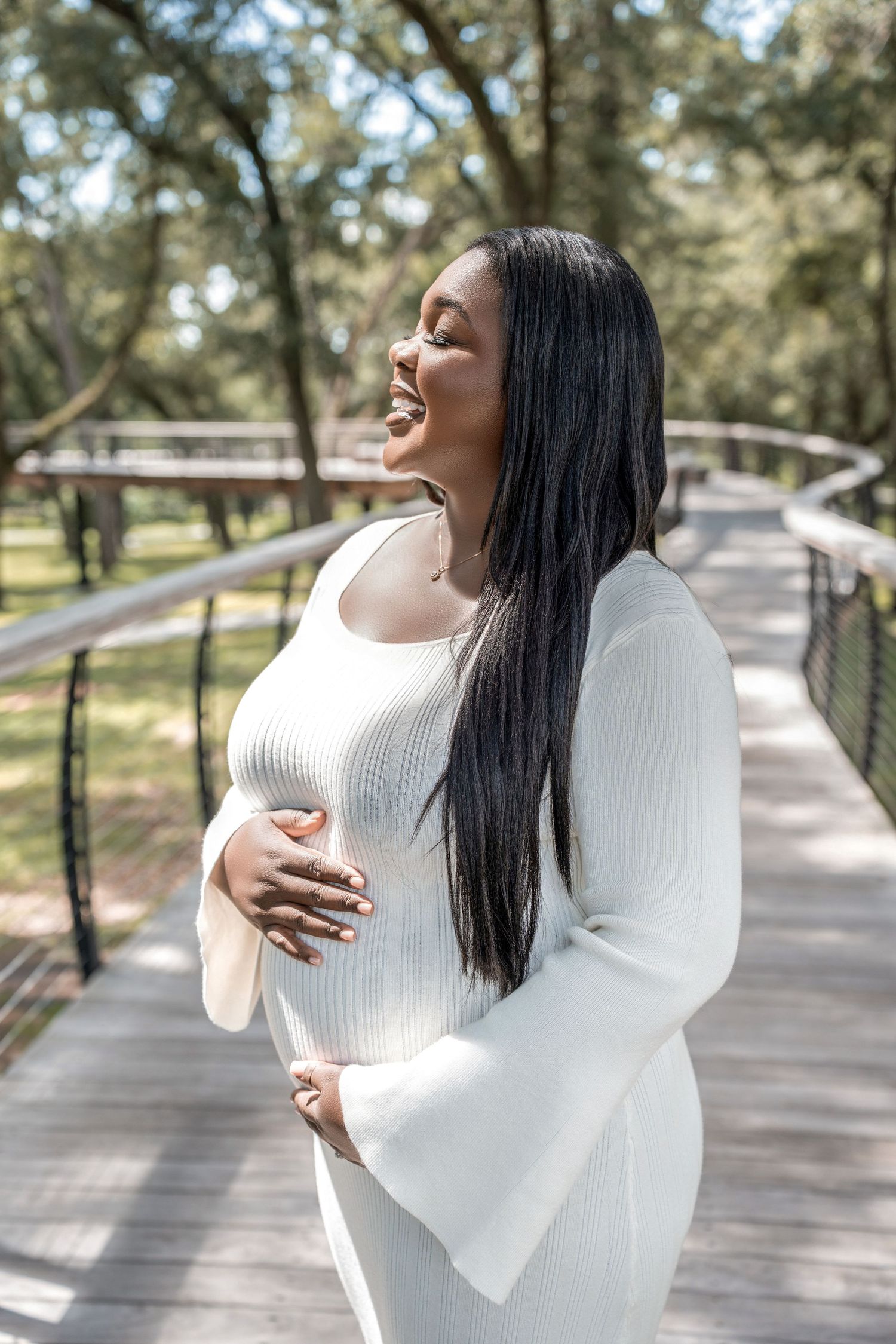 Woman in white sweater laughing and posing on wooden bridge in sunny outdoor park setting.