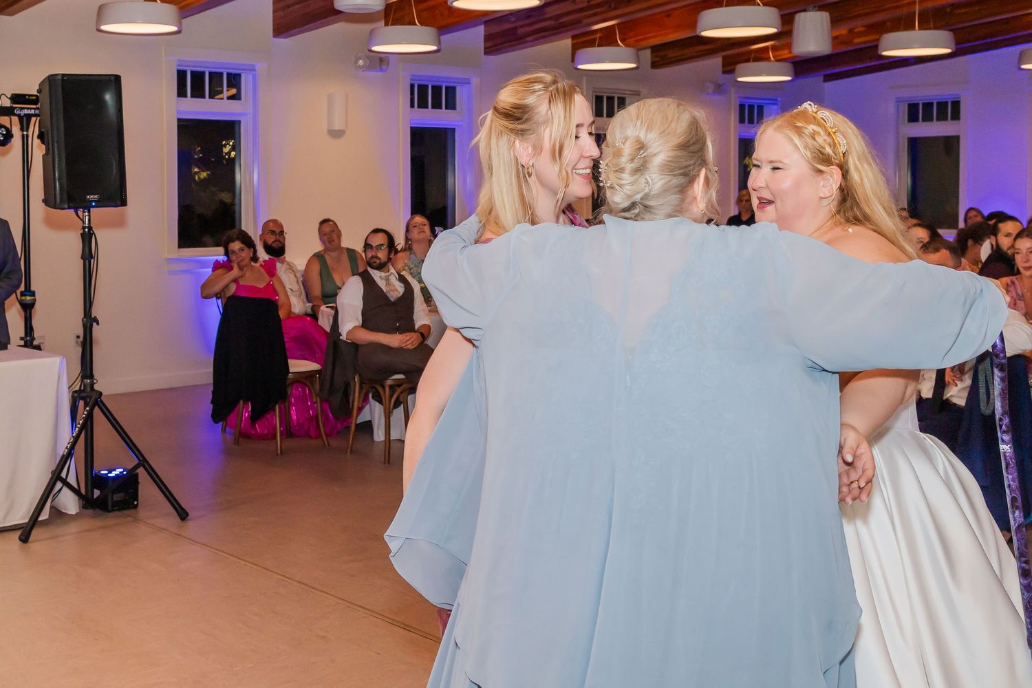 Couples dancing together at a wedding reception in a large hall with purple accent lighting.