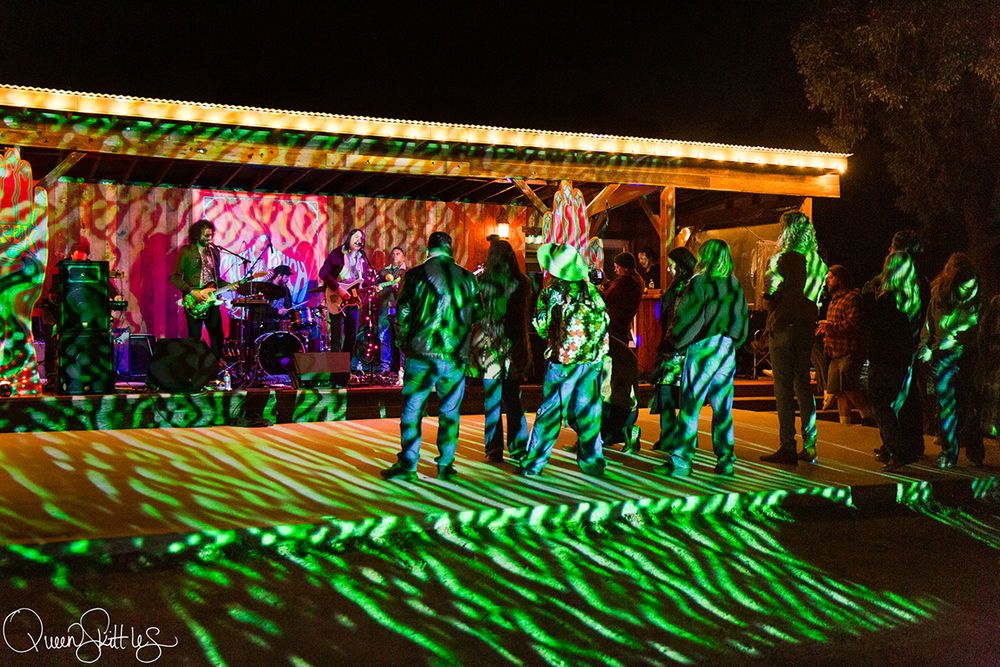Outdoor night concert with green laser lights illuminating dancers on a wooden stage at a lively music festival.