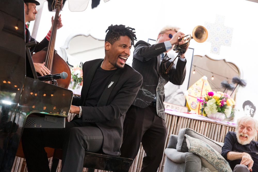 A young Black musician in a black suit laughs joyfully while performing with a jazz band at an elegant event.