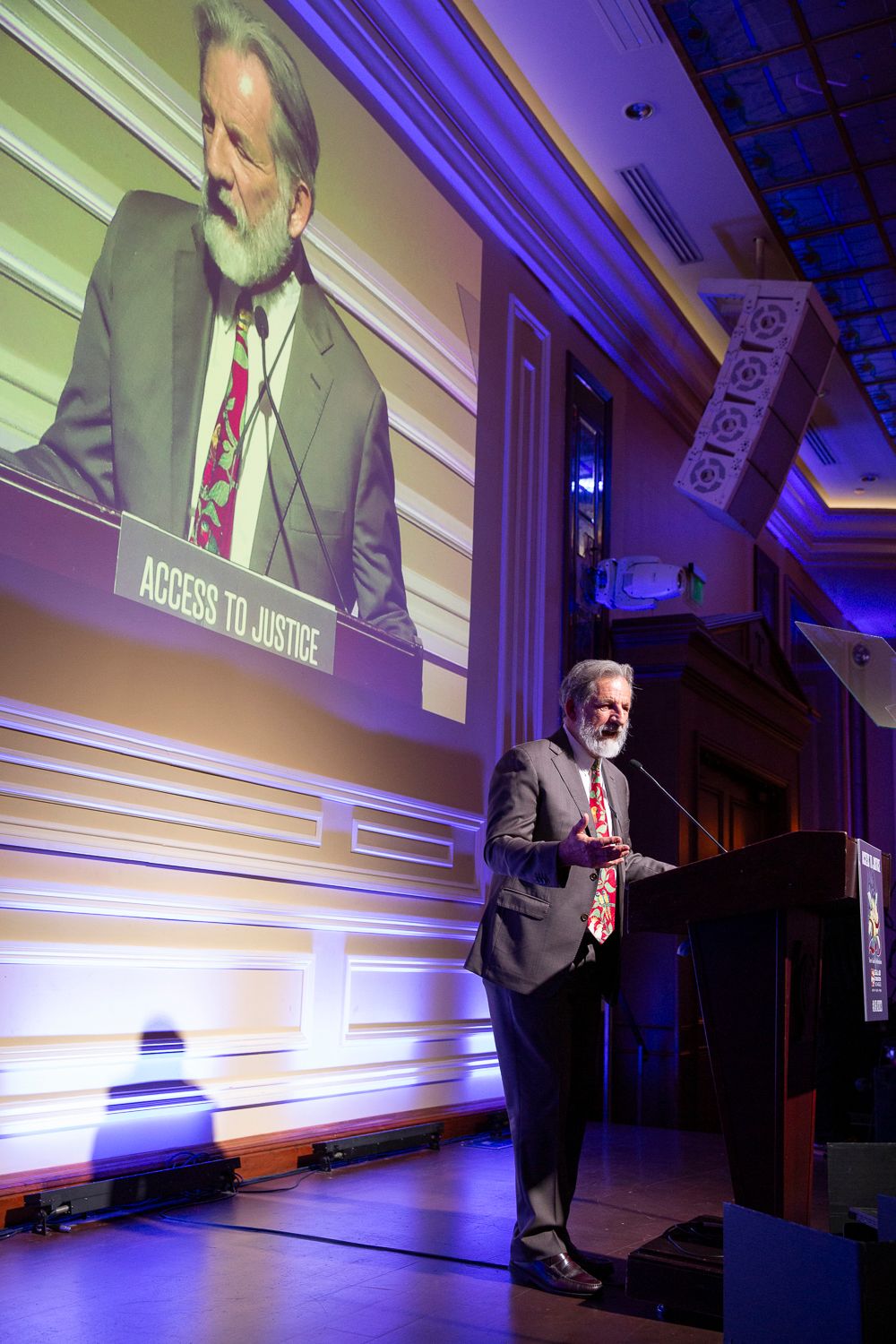 Speaker presenting on stage at a conference with dramatic blue and purple lighting effects.