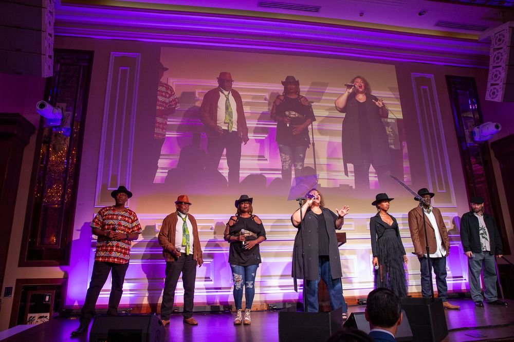 A row of silhouettes of people dancing in a purple-lit room with a large projection screen in the background.