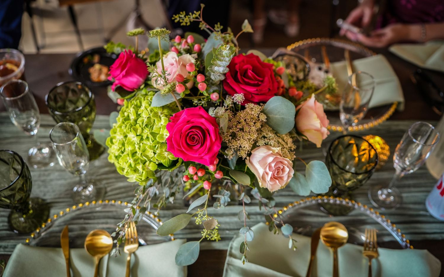 Elegant floral centerpiece with red, pink roses and green hydrangeas on a decorated dining table with gold cutlery.