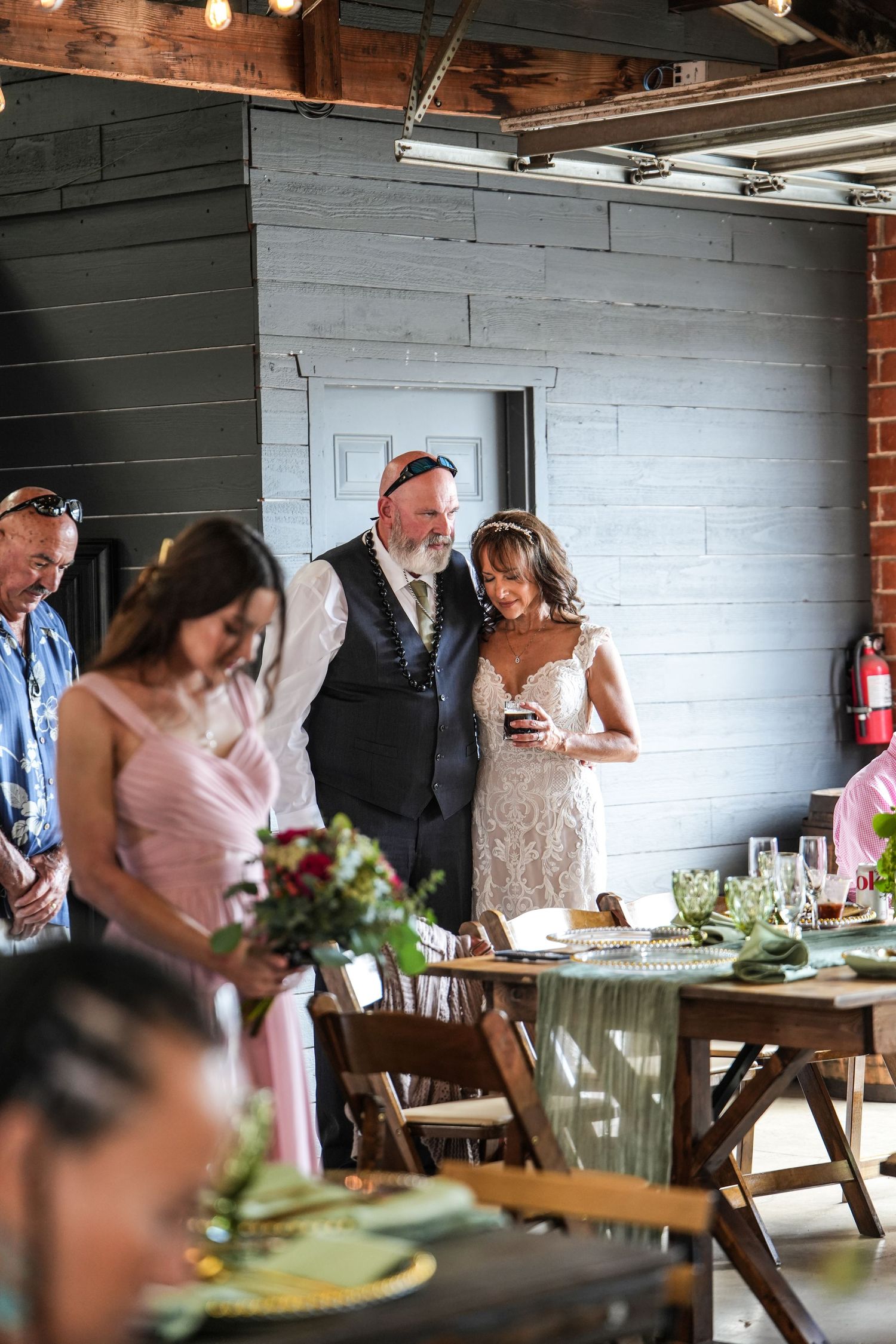 Bride and groom smiling together at rustic indoor wedding reception with wooden tables and floral centerpieces.