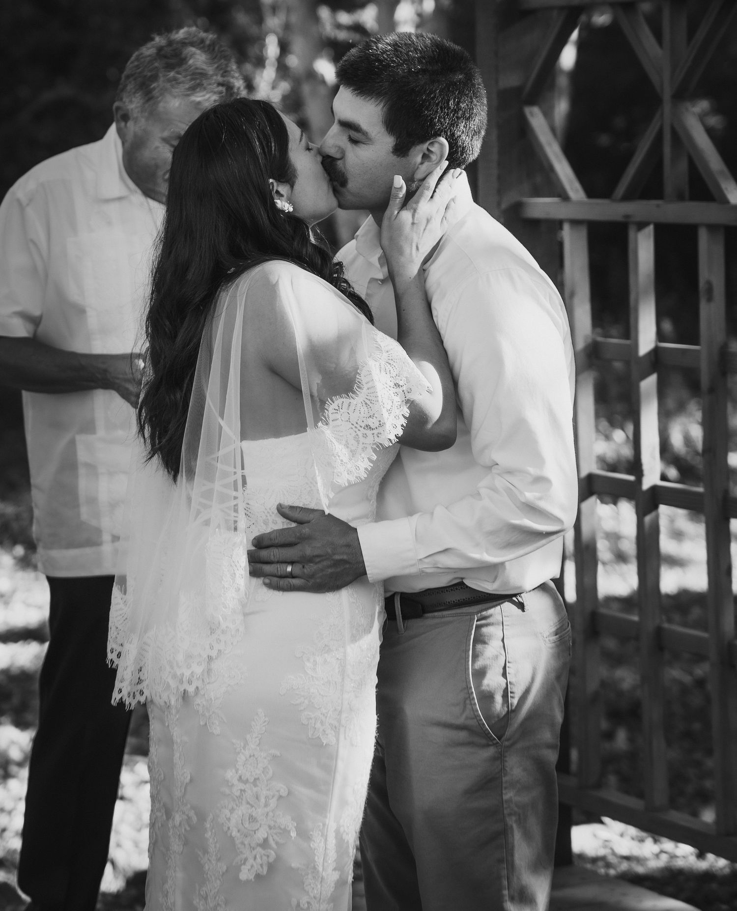 Black and white photo of a bride and groom sharing their first kiss during an outdoor wedding ceremony.