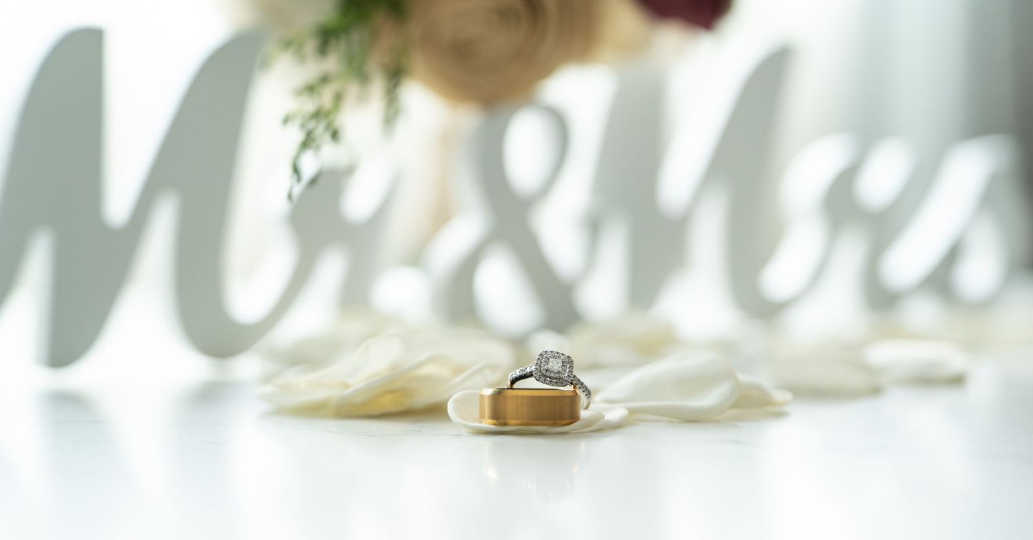 Wedding rings displayed on a small wooden box in front of a decorative Mr. & Mrs. sign with floral arrangement.