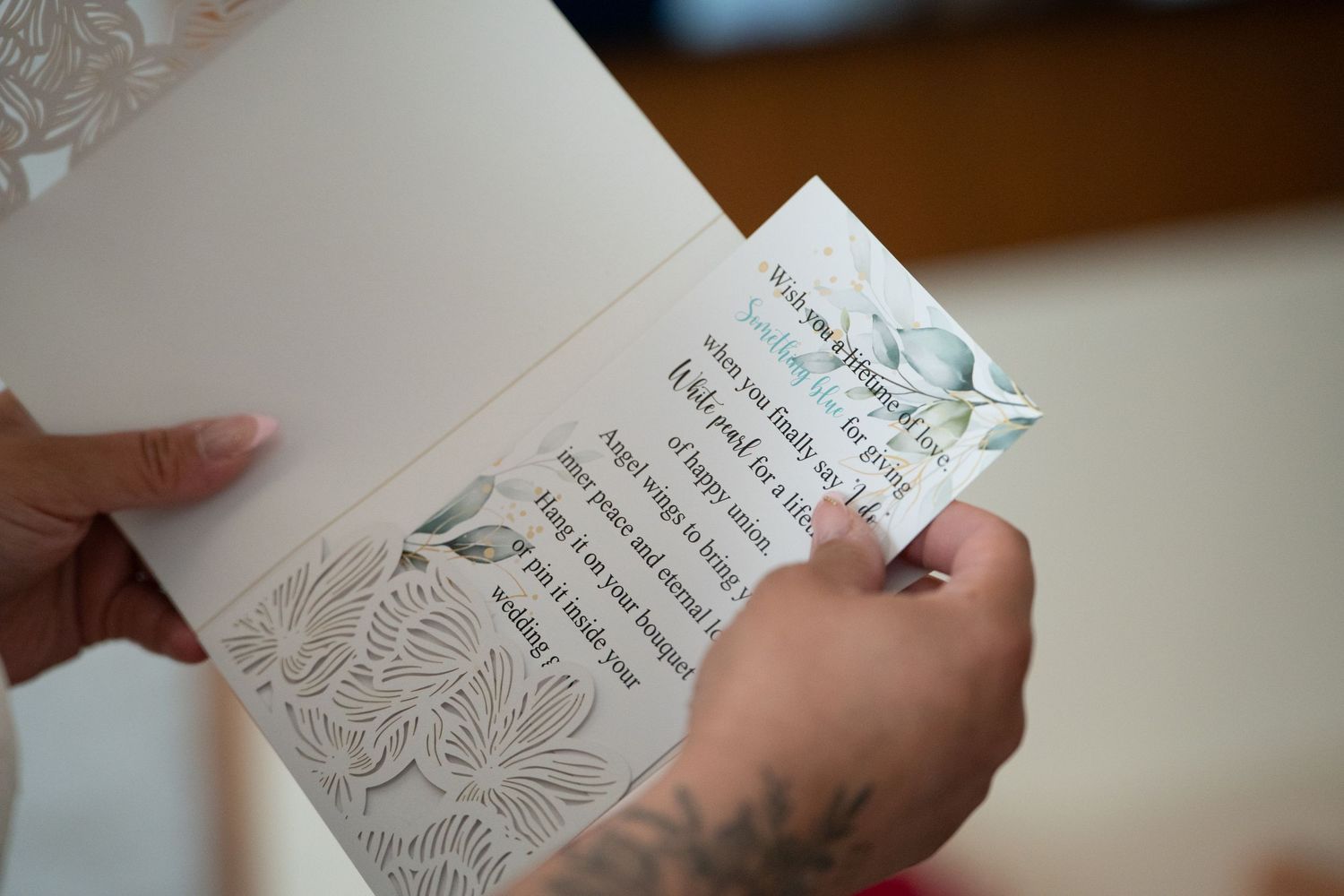 Hands holding an open greeting card with elegant floral embossed design and heartfelt printed message inside.