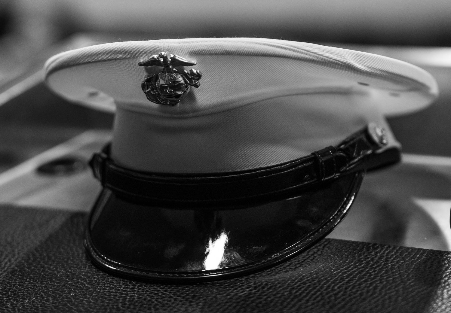 Black and white photo of a US Marine Corps dress cap with eagle globe and anchor emblem on a dark surface.