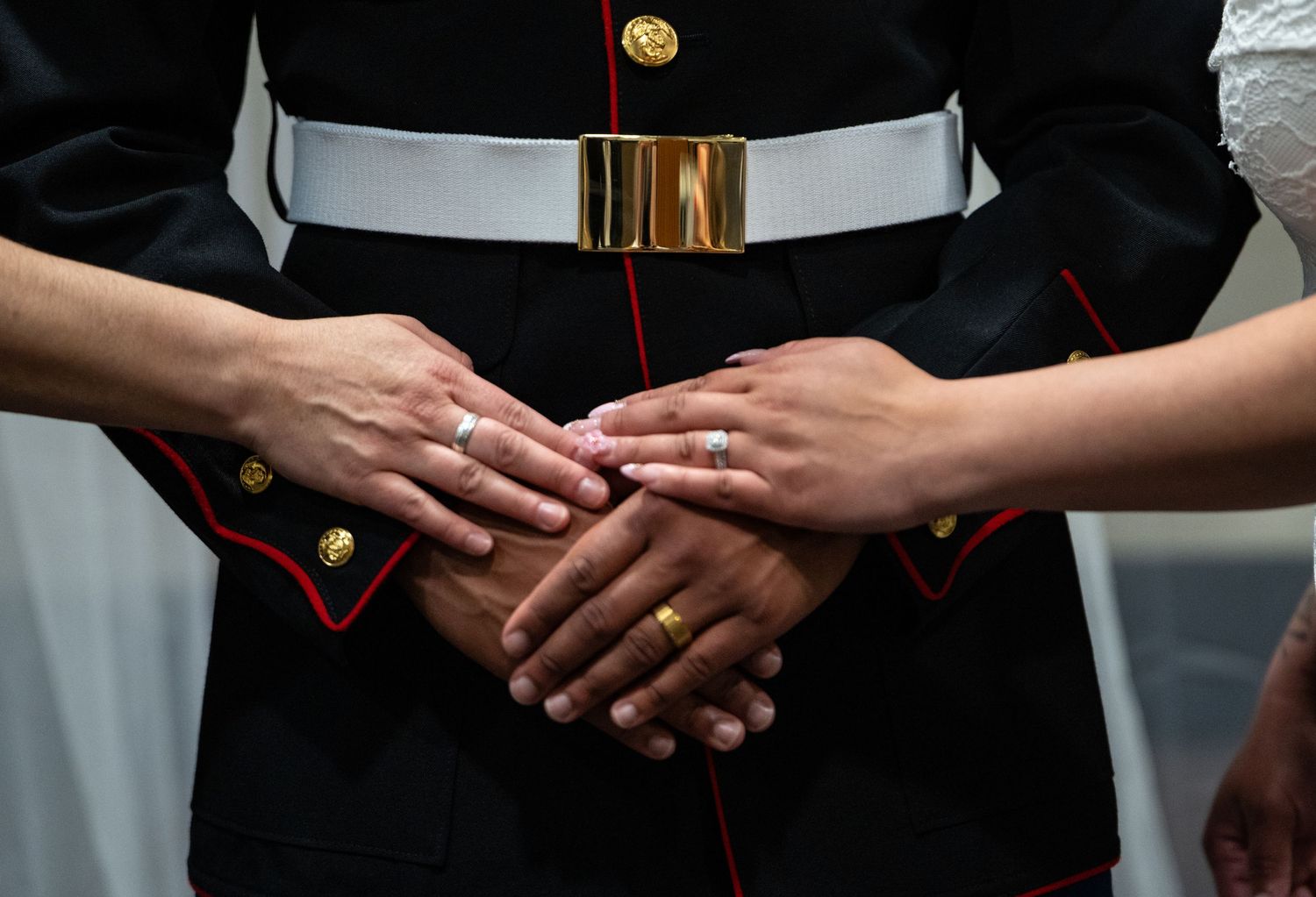 Marine in dress uniform with hands joined showing wedding rings during ceremony.