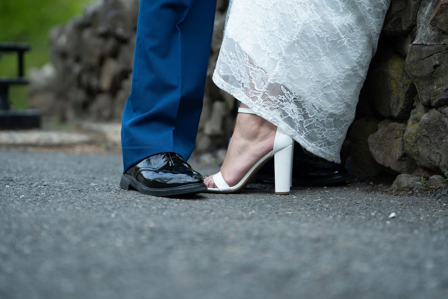 Close-up of wedding couple feet, groom in black dress shoes and blue suit, bride in white heeled sandals and lace gown.