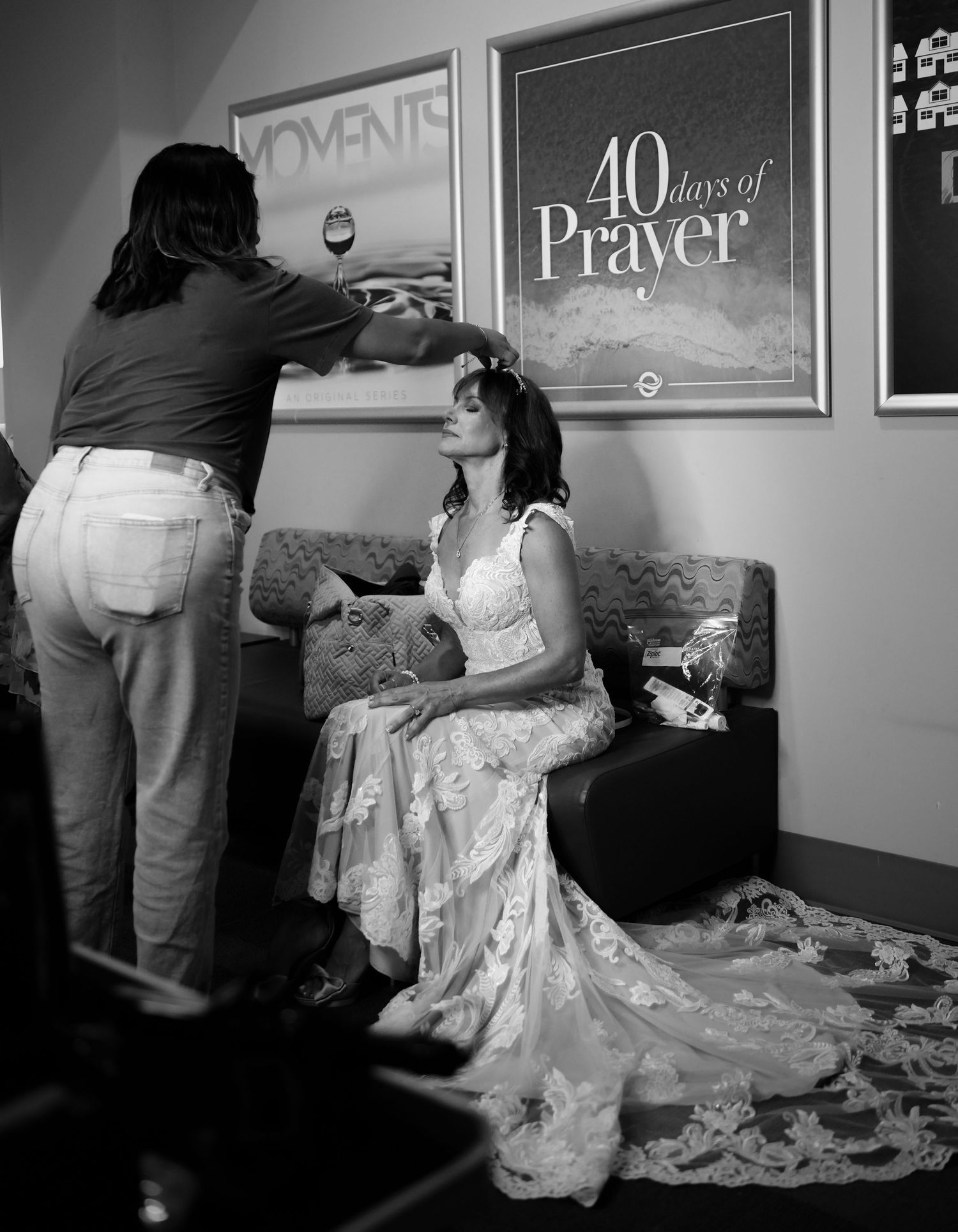 Black and white photo of a stylist adjusting a brides hair as she sits in a wedding dress before ceremony. San Diego County
