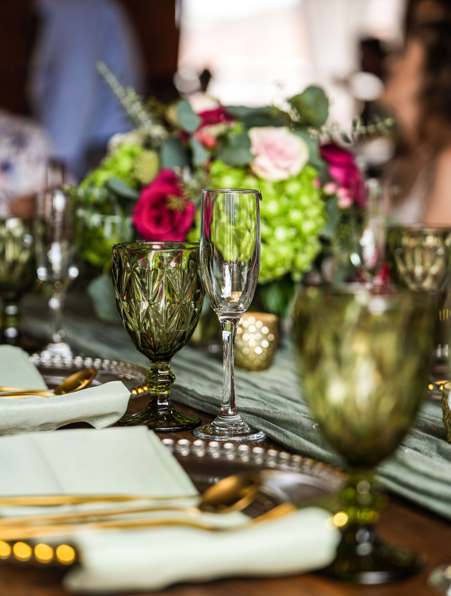 Close-up of a wedding reception table with green goblets, champagne flutes, and floral arrangements.