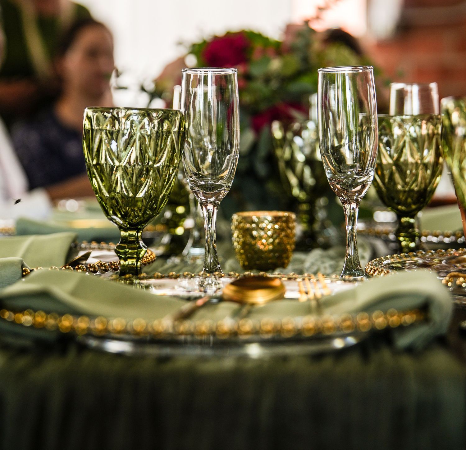 Elegant wedding table setting with green glassware, gold accents, and floral centerpieces.